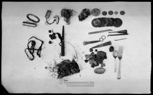 Contents of bag including oracle disks, fire-strikers, tinder, a pipe, sinew, a European fork and spoon, scrapers, drills, a cigarette butt, possibly tobacco, and possibly tsi, next to a ruler for measurement