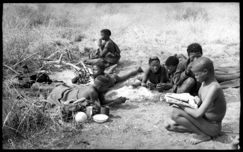 "/Qui Hunter" lying down on the left with ≠Toma and other unidentified people around him