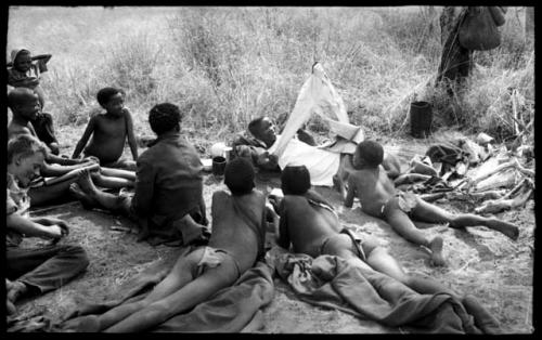 "/Qui Hunter" putting on clothes while ≠Toma, John Marshall, and other unidentified people watch