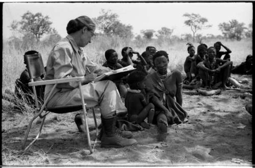 Lorna Marshall taking notes, !Ungka Norna seated next to !U, /Naoka ("Gao Medicine's" first wife) and other unidentified people in the background