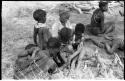 Group of women and children including !Ungka and an unidentified woman removing ornaments from /Khoa (/Qui's daughter)