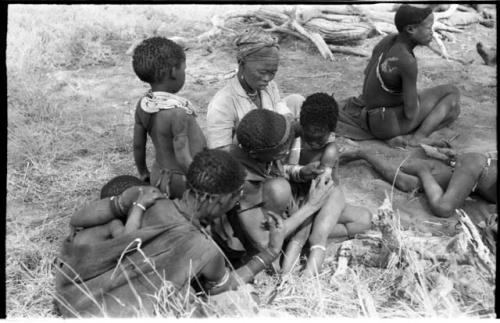 Group of women and children including !Ungka and an unidentified woman removing ornaments from /Khoa (/Qui's daughter)