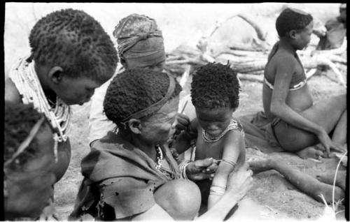 Group of women and children including !Ungka and an unidentified woman removing ornaments from /Khoa (/Qui's daughter)