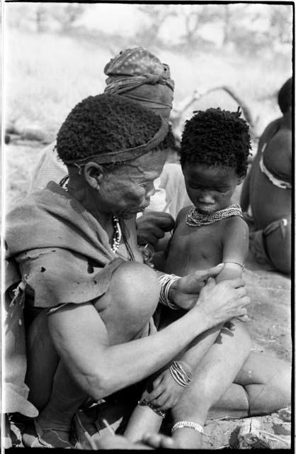 !Unkga and an unidentified woman removing ornaments from /Khoa (/Qui's daughter)