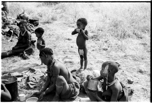 !U seated in the foreground, !Ungka Norna licking a can, an unidentified, visiting girl and Debe holding cans, and Di!ai seated in the background