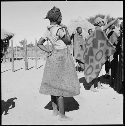 Woman standing, and another woman wearing a blanket in background