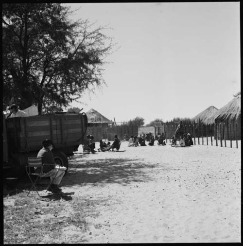 People sitting next to fence, long shot, with Laurence Marshall in foreground, and Nicholas England in truck recording