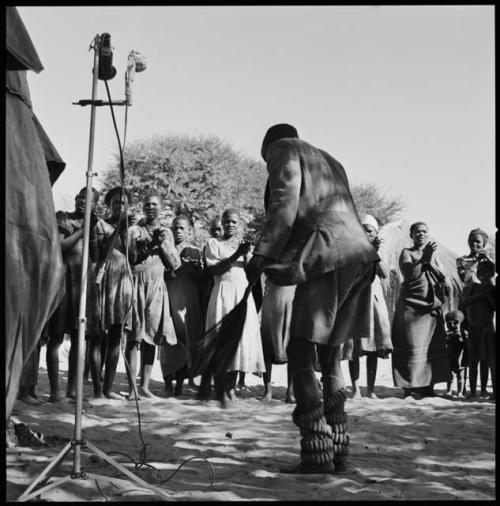 Man dancing with rattles, and women clapping