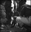 Children standing, and Lorna Marshall writing in a notebook, with Deborah Marshall next to her