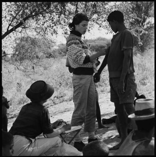 Man having his skin color documented by Deborah Marshall, and Lorna Marshall taking notes