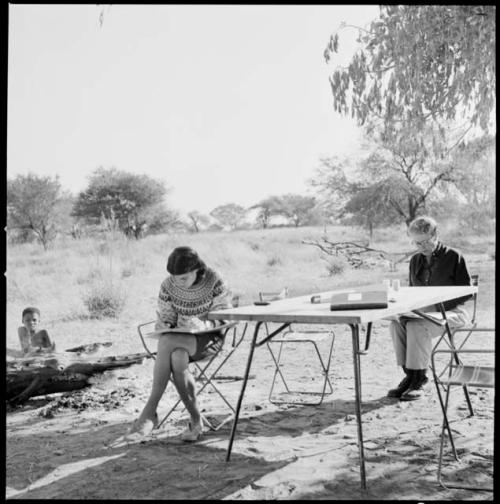 Person sitting behind Lorna Marshall and Deborah Marshall sitting at the dinner table, writing