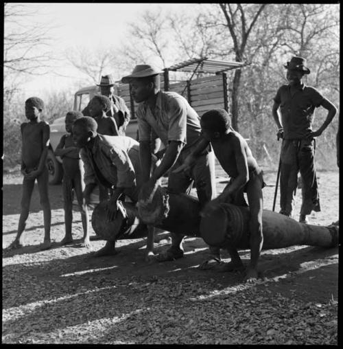 Two men and a boy playing drums, with other people standing nearby