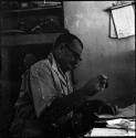 C. J. Mathias sitting at a desk looking at notebook (underexposed)