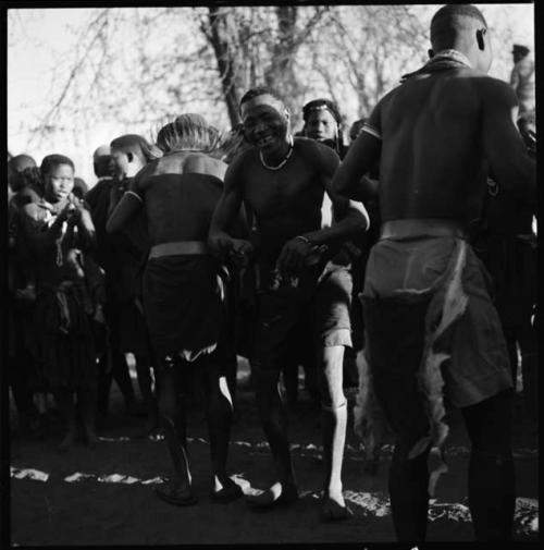 Men dancing, close-up, with group of women singing in background