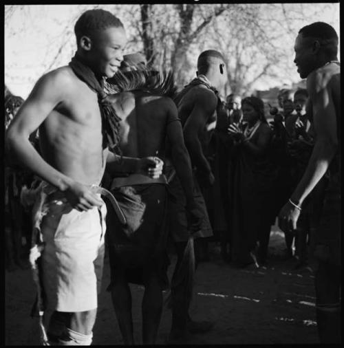 Men dancing, close-up, with group of women singing in background