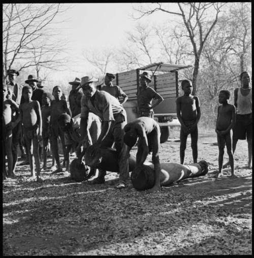 Three men playing drums, with boys and other people standing next to them