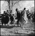 Man and woman dancing, and group singing and clapping, with expedition truck in background