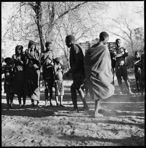 Man and woman dancing, and group singing and clapping, with expedition truck in background