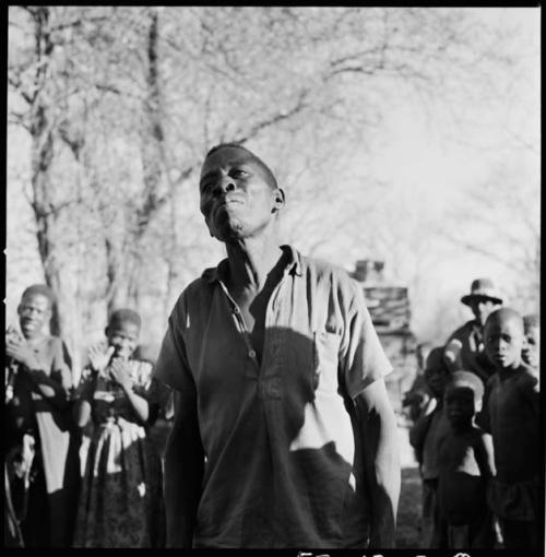 Man dancing, close-up; group of people singing and clapping in the background