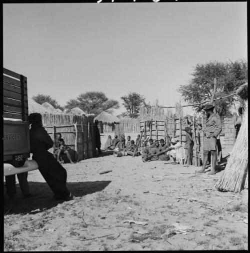 People sitting next to fences, and Kernel Ledimo standing by one of the expedition trucks