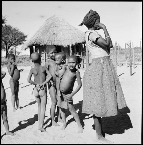 Woman standing, with children behind her and hut in background