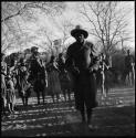 Man, possibly Ruru, wearing a big hat and dancing with group of people singing in background