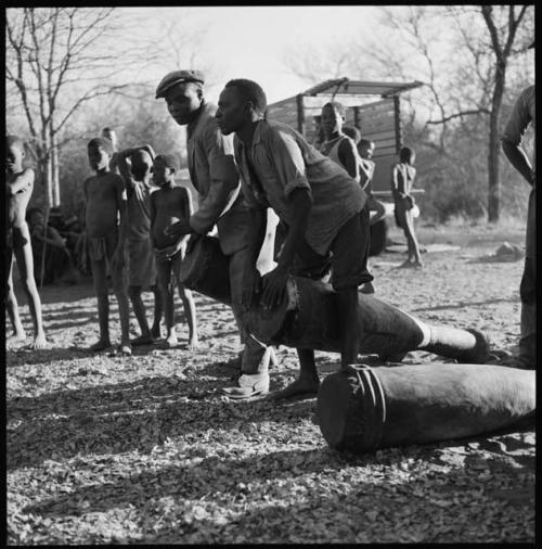 Two men playing drums, and another drum on the ground beside them