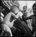 Tãõ (Daou or !Aikwe), wife of Tango (Chitango), and a baby drinking from a cup
