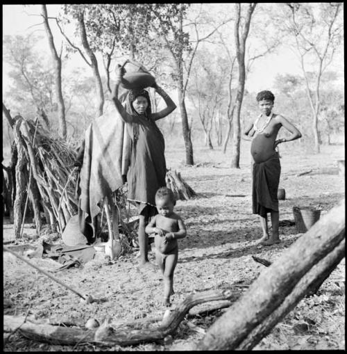 //Nui, wife of Naka, standing next to a baby and a woman carrying a basket on her head