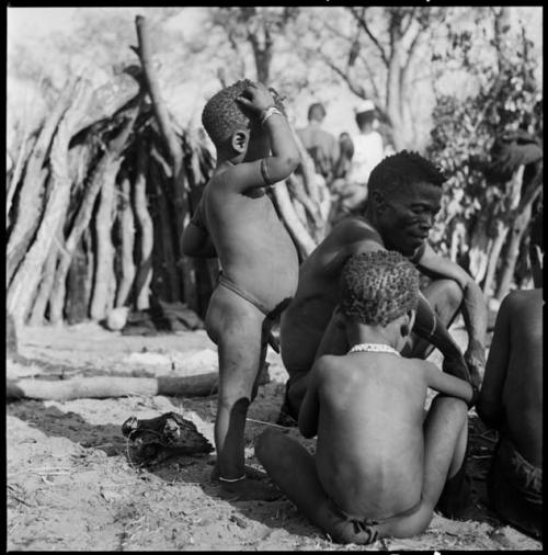 Kumsa sitting, with children sitting and standing next to him