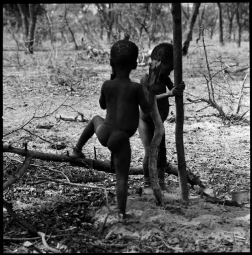 Two children standing, and one pounding something with a long mortar stick