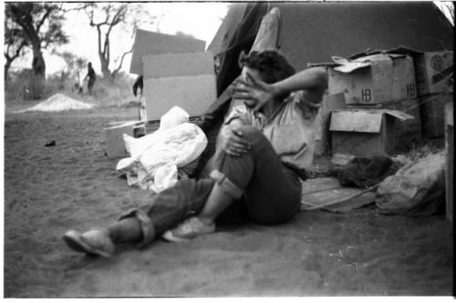 Elizabeth Marshall Thomas seated on the ground, hand blocking camera