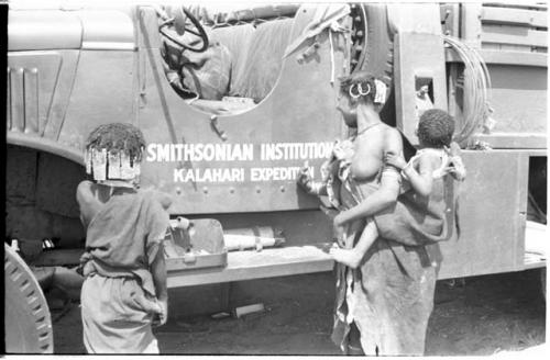 N!ai and a woman standing in front of one of the expedition's GMC trucks with "Smithsonian Institution Kalahari Expedition" showing