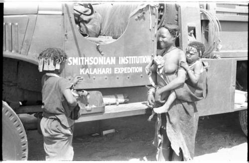 N!ai and a woman standing in front of one of the expedition's GMC trucks with "Smithsonian Institution Kalahari Expedition" showing