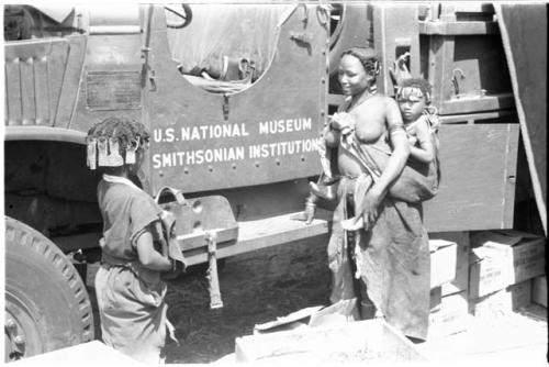 N!ai and a woman standing in front of another GMC truck with "U.S. National Museum, Smithsonian Institution" showing