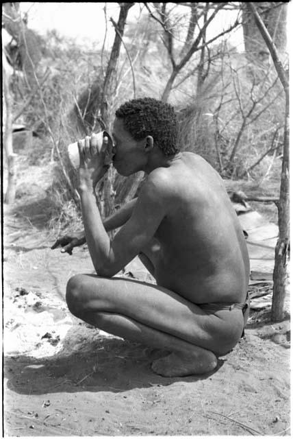 "/Qui Navel" squatting, drinking from a tin