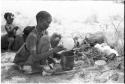 /Naoka, first wife of "Gao Medicine," emptying an ostrich egg into a pot, with child sitting on somebody's back behind her