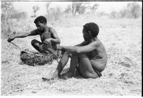 Man watching ≠Toma lining a carrying net with a small kaross to pack it with rattles, ostrich eggshells, etc.