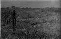 "Crooked /Qui" standing in brush, with his quiver, spear, bow, and arrow, distant view