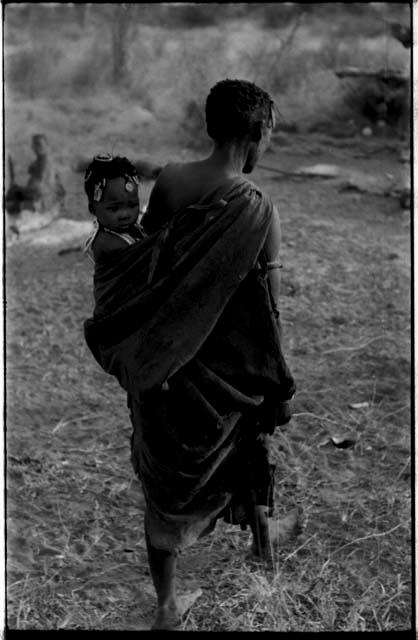 Woman walking with a baby in her kaross, seen from the back