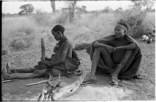 "Old /Gasa" sitting, legs straight out, pounding something with mortar and pestle; her grandson sitting beside her