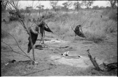 Hunting bags hanging in branches, with a bed, and a fire in the background