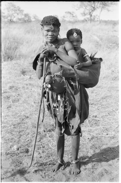 !Ghia (second wife of "Old ≠Gao" from band 10) leaning on a long stick with an unidentified child on her back, full figure standing