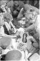 Kernel Ledimo and Lorna Marshall examining ostrich eggshell beads spread on a sandal, with a group of people watching them