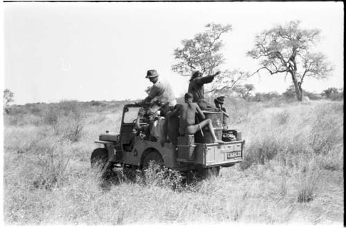 Expedition members and Ju/'hoansi riding on a Jeep