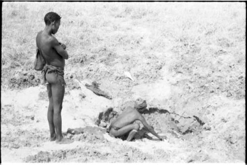 "/Gao Music" filling ostrich eggshell at a waterhole, with "Crooked /Qui" watching