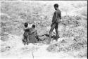 Woman filling eggshell in a waterhole; "Crooked /Qui" and an unidentified child standing behind her