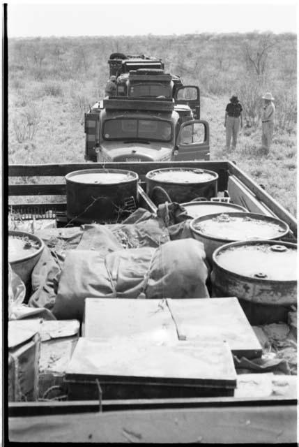 Top of expedition GMC, with trucks behind in a line; Lorna Marshall and Laurence Marshall standing beside trucks