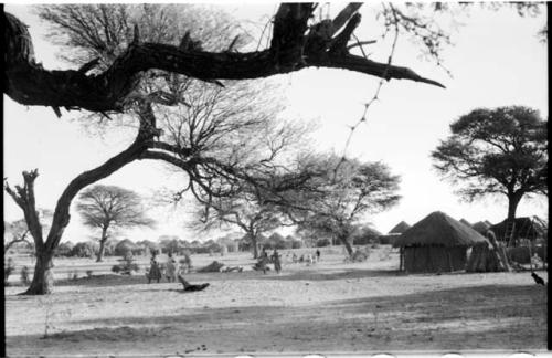 Women walking, and a group sitting, with huts in the distance