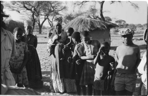 Group of people standing, with huts in background